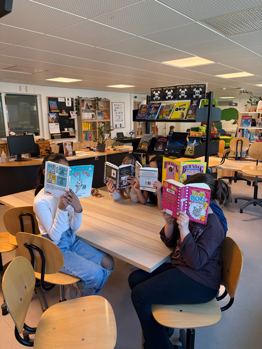 En gruppe mennesker som sitter ved pulter og leser bøker