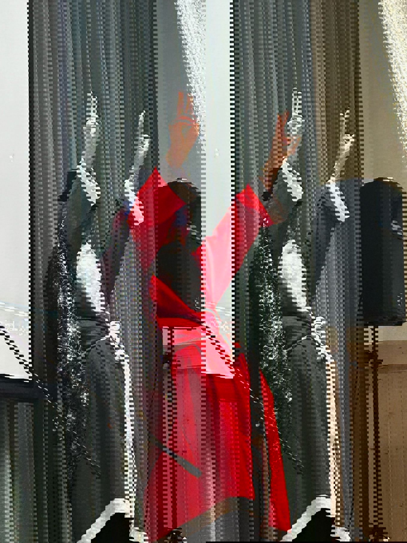 en person i rød kappe og hatt med hendene opp