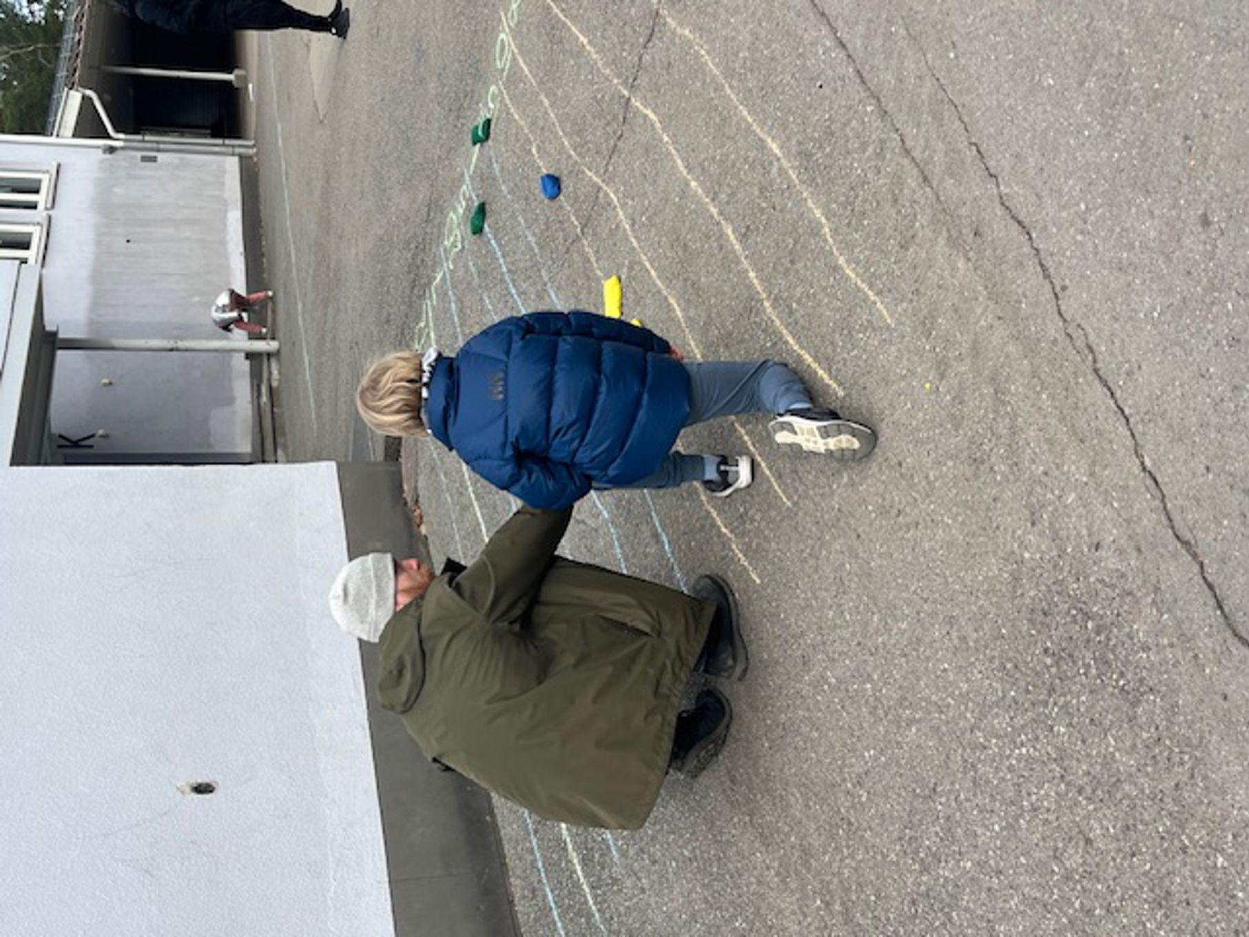 Foto: Anne Roland en person og et barn som leker med leker på en betongoverflate